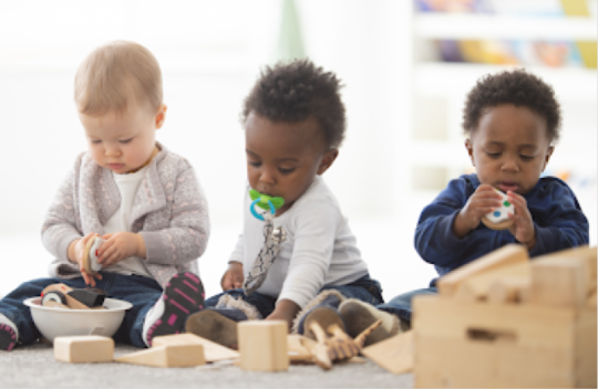 3 children sitting in a row looking at and playing with toys