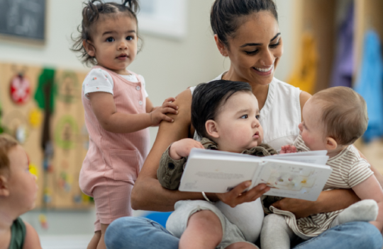 A photo of an adult sitting with three young children and reading a book