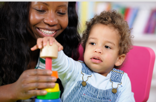 Photo of an adult with a young child who is playing with a toy